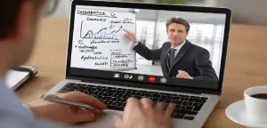 Business-professional-participates-in-a-focused-video-learning-session-demonstrating-growth-trends-on-whiteboard-while-actively-taking-notes-on-a-laptop